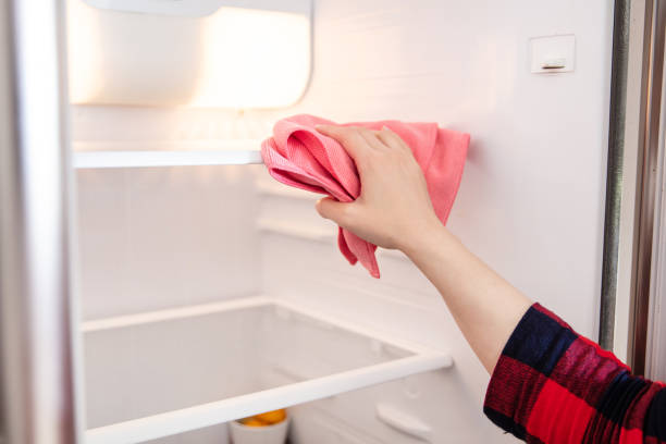 Woman removing shelves to clean a fridge interior with bicarbonate of soda.
